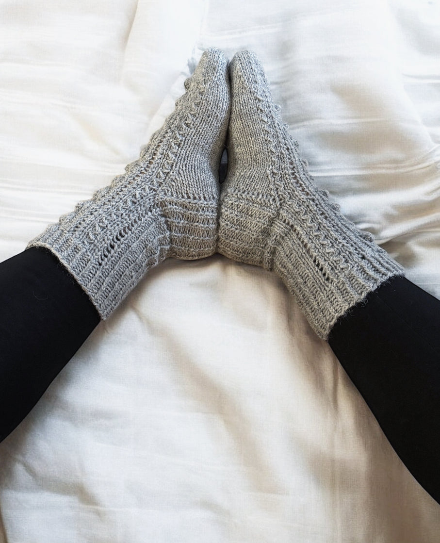 Talvipäivä villasukat. Pitsiä, palmikkoa ja nyppyjä. Neuleohje saatavilla NordicKitty verkkokaupasta.